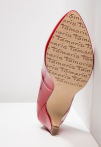 Chaussure à talon haut rouge inclinée vers le haut montrant la semelle beige embossée du logo "Tamaris" répété et la marque de taille 37.