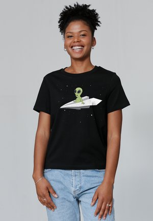 Zwarte katoenen t-shirt met een groene buitenaardse grafiek die op een zilveren papieren vliegtuigje zit, tegen een sterrenachtergrond. Korte mouwen, relaxte pasvorm.
