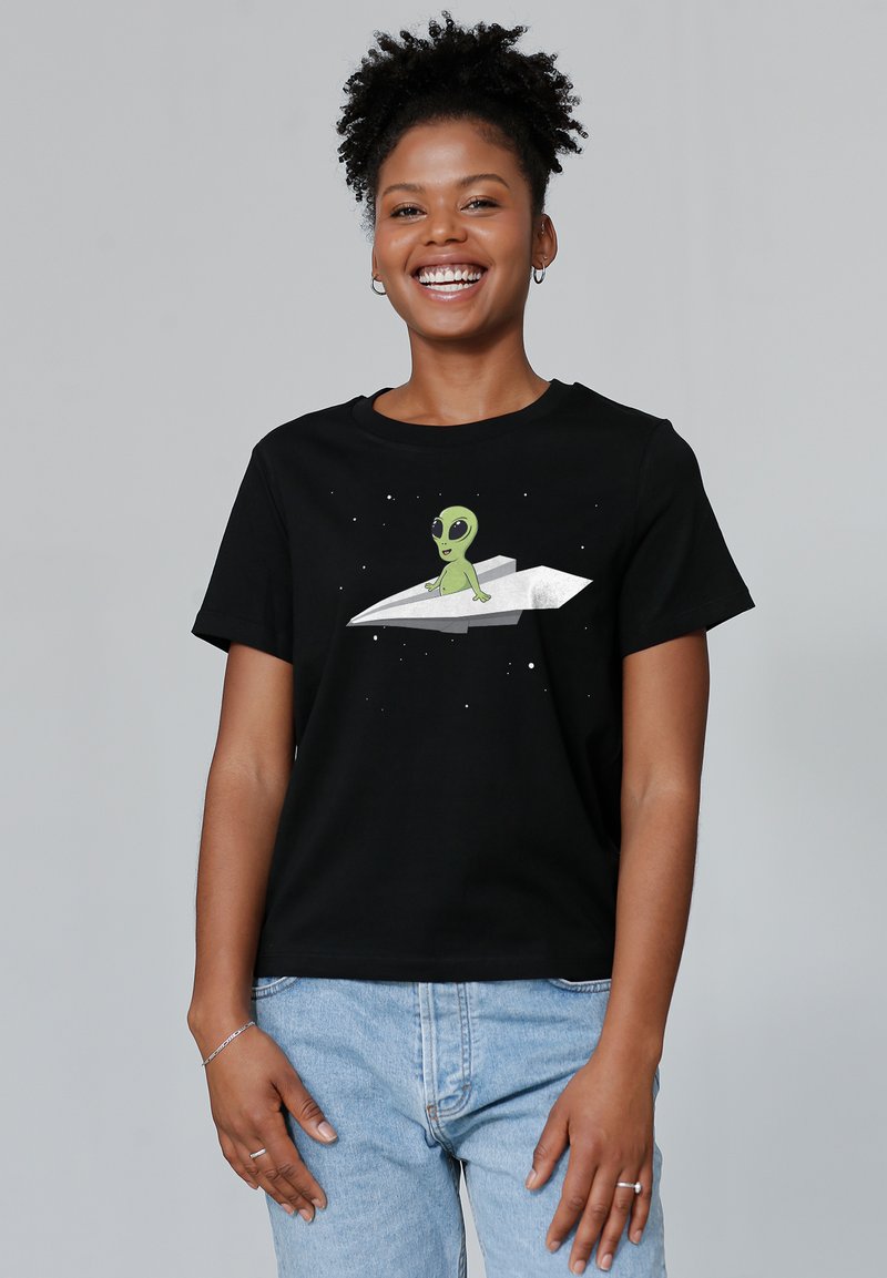 Zwarte katoenen t-shirt met een groene buitenaardse grafiek die op een zilveren papieren vliegtuigje zit, tegen een sterrenachtergrond. Korte mouwen, relaxte pasvorm.
