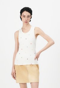 Witte geribde tanktop met kleurrijke bloemapplicaties, gecombineerd met een lichtgele minirok. De outfit heeft een aansluitend ontwerp en een mouwloze stijl.