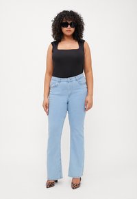 Bodysuit negro de escote cuadrado, jeans acampanados de color azul claro, gafas de sol negras y zapatos de tacón con estampado de leopardo, usados por una persona con cabello rizado.
