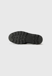 Black rubber shoe sole with a rugged design, featuring deep treads and raised accents for traction. Flat, oval shape with visible branding.
