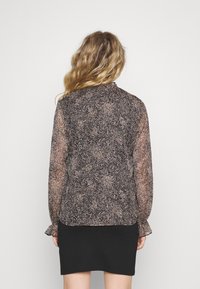 Blouse à motifs noirs et roses avec de longues manches transparentes, un col à boutons et des poignets volantés, associée à une jupe noire unie.