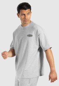 Camiseta de algodón gris con mangas cortas, cuello redondo y un pequeño logo ovalado en el pecho. Textura suave y corte relajado.