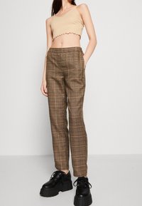 Haut court beige avec des bords festonnés, assorti à un pantalon à carreaux marron offrant une texture lisse et des poches latérales. Chaussures plateformes noires.