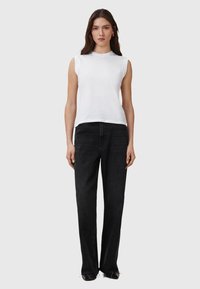 Weißes ärmelloses Oberteil, kombiniert mit hochgeschnittenen schwarzen Jeans; glattes Material, lockere Passform, gerade Beine, subtile Textur und minimale Details.