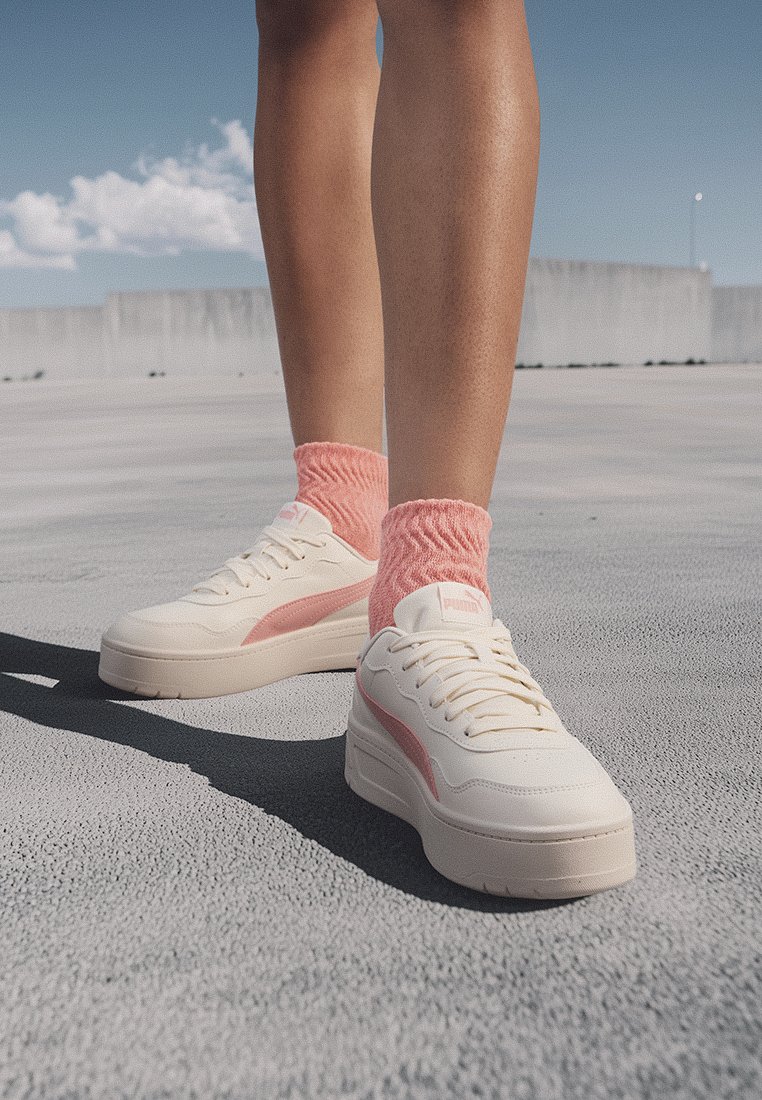 Puma-Sneaker in Creme mit pinken Akzenten, im niedrig geschnittenen Design, mit strukturierten Schnürsenkeln und einer dicken Sohle. Getragen mit pinken Scrunch-Socken.