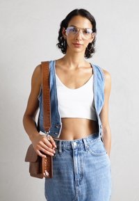 Gilet en jean sans manches, crop top blanc, jean taille haute bleu clair, et un sac en bandoulière marron avec une finition texturée.