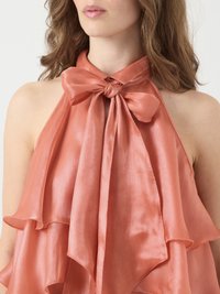 Top halter in satin pesca con fiocco al collo, caratterizzato da rouches sovrapposte e una texture liscia. Il design elegante enfatizza il flusso e la caduta.
