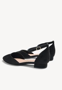 Chaussures pour femmes en daim noir à talons bas, bouts pointus et brides à la cheville avec boucles dorées sur fond blanc.