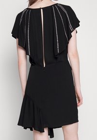 Black dress with flutter sleeves, adorned with silver studs along the back. Features a keyhole opening and a ruffled hemline.