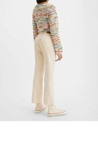 Pull en crochet avec des rayures multicolores associé à un jean droit beige clair ; modèle portant des baskets montantes claires.