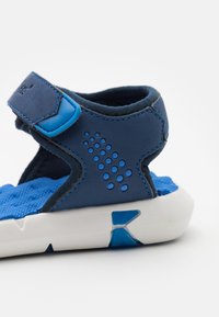 Sandal blu con tomaia texturizzata, cinturino regolabile e suola bianca. Presenta fori di ventilazione e un interno imbottito per il comfort.