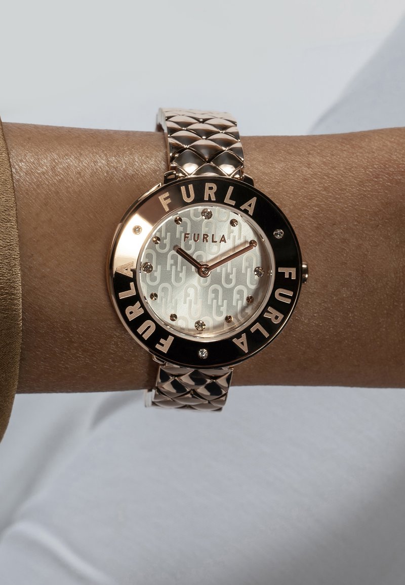 Rožu zelta pulkstenis ar rakstu ciparnīcu, melnu rāmīti ar iegravētu "FURLA" un teksturētu siksniņu ar kvadrātveida dizainu.