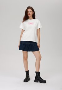 Camiseta blanca de algodón con un gráfico de corazón con un lazo rosa, combinada con una minifalda de mezclilla oscura acampanada y botas negras de tobillo con hebillas.