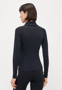Maglia sportiva nera a manica lunga realizzata in tessuto testurizzato, con collo alto e vestibilità aderente, dotata di cuciture piatte per il comfort.