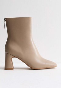 Beige leren enkelboot met een puntige teen en een blokhak. Zijrits voor sluiting en een gladde textuur, geschikt voor veelzijdige styling.