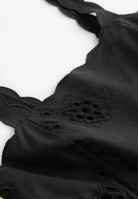 Blusa nera senza maniche con motivi floreali ricamati e bordi scallop. Realizzata in tessuto liscio con una consistenza morbida.