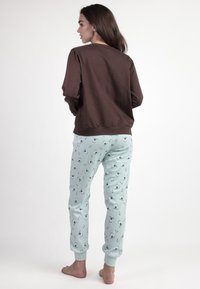 Camisa de manga larga marrón combinada con pantalones de pijama verde menta claros con un estampado de pingüinos; tejido suave, corte casual, puños elásticos.