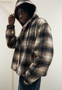 Brun och beige rutad zip-up huvtröja med en mjuk textur, med svarta dragsnören och sidofickor, kombinerad med en ljus polokrage.