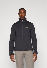 Giacca nera con zip e colletto alto, realizzata in tessuto morbido. Presenta una cucitura sul petto e un logo decorativo, progettata per il comfort e la funzionalità.
