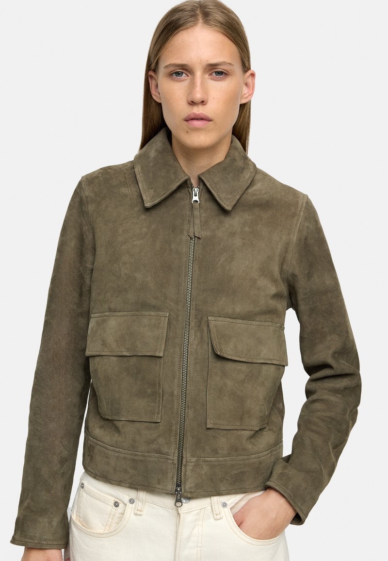 Oliwkowa zamszowa kurtka z zamkiem błyskawicznym, dwoma przednimi kieszeniami i kołnierzem do opadania. Gładka tekstura, skrócony krój.