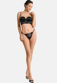 Ensemble de lingerie noire comprenant un soutien-gorge en satin avec des accents en dentelle et un armature, accompagné d'un string en dentelle assorti avec de fines bretelles.