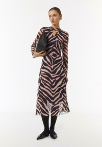 Robe à manches longues avec un motif zèbre rose et marine. Découpe en forme de clé au cou et silhouette fluide. Associée à un sac noir et des chaussures plates.