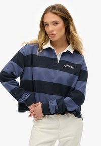 Polo de manga larga a rayas en tonos azul marino y azul, con cuello blanco y el logo "Superdry" bordado en el pecho.
