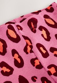 Tela de pana rosa con un audaz estampado de leopardo. Figuras en rojo oscuro y naranja contrastan con el fondo texturizado en rosa.