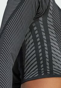 Top atletico nero con strisce diagonali e orizzontali grigie a contrasto. Il tessuto presenta una finitura liscia e testurizzata con un design aderente.