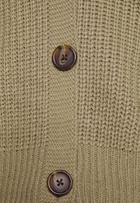 Khaki pletený cardigan s texturou s vertikálními pruhy, zdobený hnědým knoflíkem s jemným mramorovým vzorem.