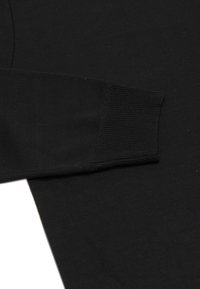 Maglietta nera a maniche lunghe con polsini a coste e una texture liscia, dal design aderente e con cuciture minime visibili.