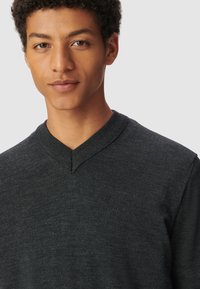 Ciemnoszary sweter z dekoltem w serek, wykonany z teksturowanej tkaniny, z prążkowanym kołnierzem i dopasowanym krojem, charakteryzujący się gładką, równą powierzchnią.