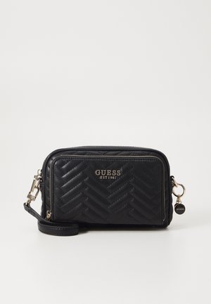 Zwarte doorgestikte crossbodytas met "GUESS EST 1981" logo, voorvak met rits, goudkleurige hardware en afneembare polsband.