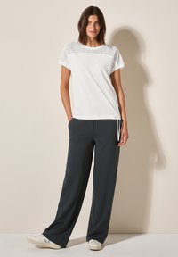 Haut blanc à manches courtes avec des détails en mesh, associé à un pantalon large noir et des baskets blanches. Tissu doux avec une taille élastique.