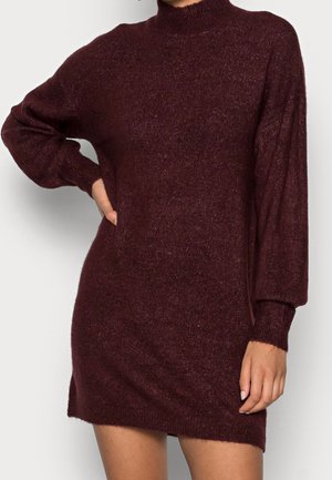 Robe-pull bordeaux en maille avec col montant, manches longues et coupe ample. Texture douce et poignets côtelés ajoutent du détail au design.