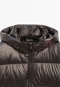 Giacca a vento imbottita marrone scuro con collo alto, texture lucida, chiusura con cerniera visibile e motivo trapuntato, caratterizzata da una struttura leggera.