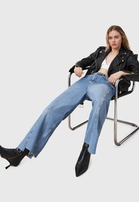 Giubbotto biker in pelle nera, top bianco aderente, jeans a gamba larga light blue a vita alta con orlo sfilacciato e stivaletti neri con punta.