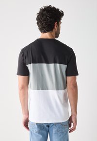 Tricou cu mânecă scurtă, cu un design în blocuri de culoare, în culorile negru, gri și alb. Fabricat din bumbac, având guler rotund și o textură moale.