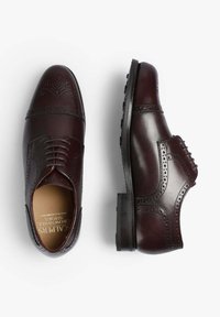 Zapatos brogue de cuero burdeos con perforaciones decorativas, presentan una puntera redonda, diseño con cordones y una suela de goma negra texturizada.