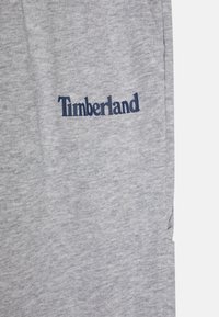 Sivé tepláky vyrobené zo soft materiálu, s námorníckym logom "Timberland" na boku. Jednoduchý dizajn s vreckami a voľným strihom.