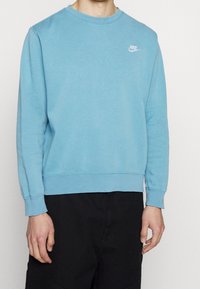 Světle modrá mikina s kulatým výstřihem, žebrovanými manžetami a lemem a malým bílým logem Nike na levé straně hrudi.