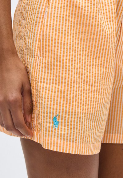 Άτομο που φοράει πορτοκαλί και λευκά κάθετα ριγωτά σορτς με ένα μικρό μπλε κεντητό λογότυπο παίκτη πόλο κοντά στο τελείωμα.