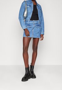 Leren jasje en bijpassende rok in lichtblauw, voorzien van klepzakken, riemdetails en een ritssluitingen aan de voorkant. Gecombineerd met zwarte enkellaarsjes.