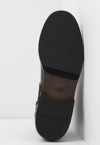 Semelle d'une chaussure habillée en cuir noir avec une semelle en caoutchouc texturée et le nom de la marque "Steffen Schraut" visible sur la semelle intermédiaire en cuir.