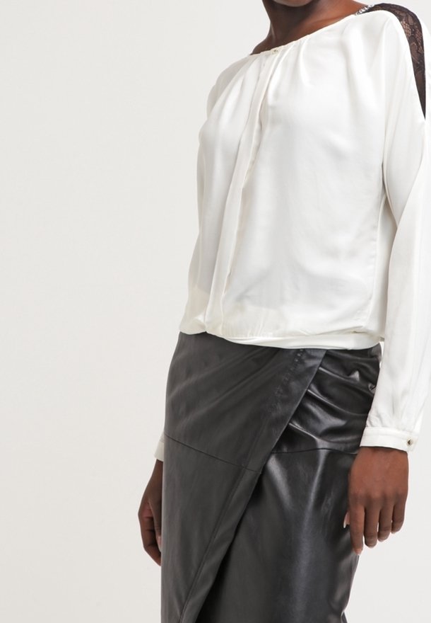 Witte zijden blouse met een gedrapeerde voorkant en zwarte kanten details op één schouder, gecombineerd met een zwarte faux leren wikkelrok.