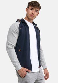 Navy and gray zip-up hoodie with a two-tone design, featuring a drawstring hood and leather accents. Soft fabric, fitted silhouette.