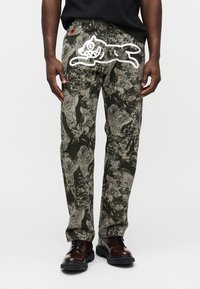 Παντελόνια με σχέδιο παραλλαγής σε αποχρώσεις του πράσινου και του γκρι, με ένα λευκό γραφικό ενός πηδώντας σκύλου στο πίσω μέρος και ανθεκτική μέση.