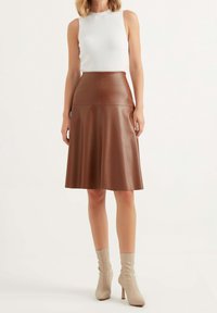 Gonna midi in pelle marrone con vita adatta e orlo a campana. Abbinata a una canotta bianca a coste e stivali con tacco alto beige.